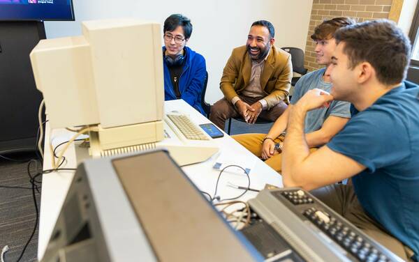 English professor Ranjodh Singh Dhaliwal shares a laugh with students as they examine a computer from the 1980s