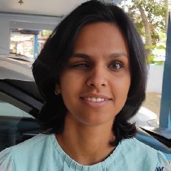 A smiling woman with short dark hair and a light blue top winks with her left eye.